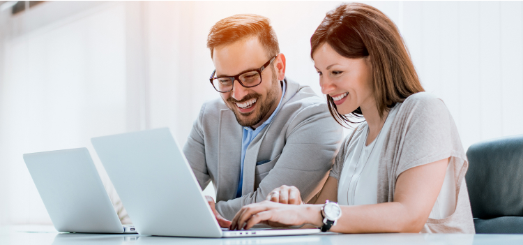 Image d’un homme et d’une femme qui sourient en regardant leurs ordinateurs