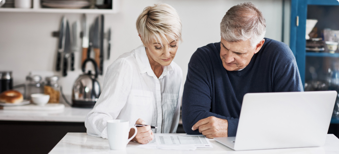 Photo of a couple looking a piece of paper and working on a computer 